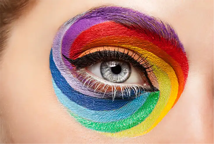 Primer plano de un ojo humano rodeado por un diseño de maquillaje artístico en forma de espiral con los colores del arcoíris, representando la psicología del color en la publicidad y el marketing visual.